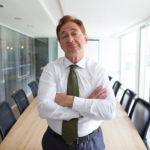 modern toplantı odasında kollarını bağlamış, kararsız ve sorgulayıcı ifadeye sahip yönetici; şirket kurucu sendromu ve liderlik kontrolü konsepti