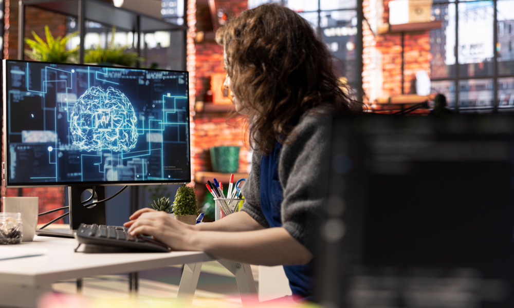 modern ofis ortamında bilgisayar başında çalışan bir kişinin ekranda yapay zekâ ve beyin ağı görselleştirmesiyle analiz yapması, yapay zekâ araçlarıyla verimli ve odaklı çalışma konsepti