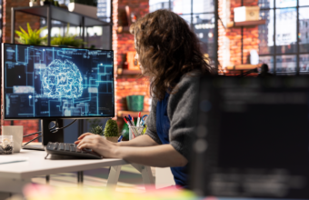 modern ofis ortamında bilgisayar başında çalışan bir kişinin ekranda yapay zekâ ve beyin ağı görselleştirmesiyle analiz yapması, yapay zekâ araçlarıyla verimli ve odaklı çalışma konsepti