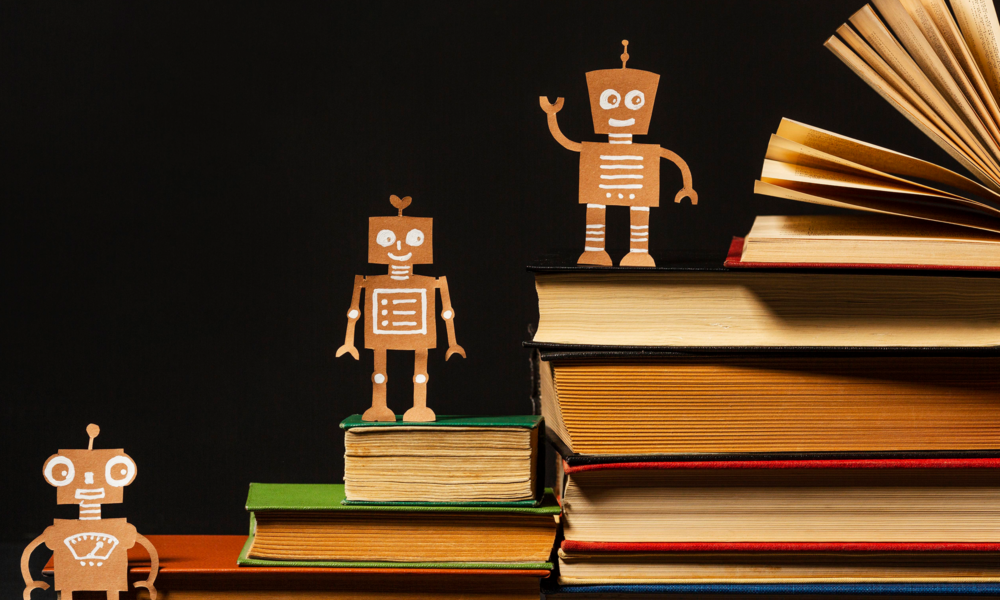kitap yığınları üzerinde duran sevimli robot figürleri, yapay zekâ okuryazarlığını ve bilgiyle gelişen teknolojiyi simgeleyen konsept görsel