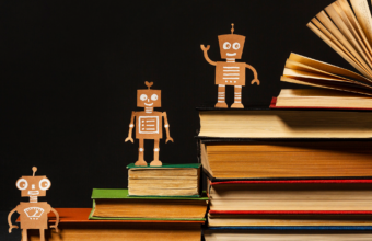 kitap yığınları üzerinde duran sevimli robot figürleri, yapay zekâ okuryazarlığını ve bilgiyle gelişen teknolojiyi simgeleyen konsept görsel